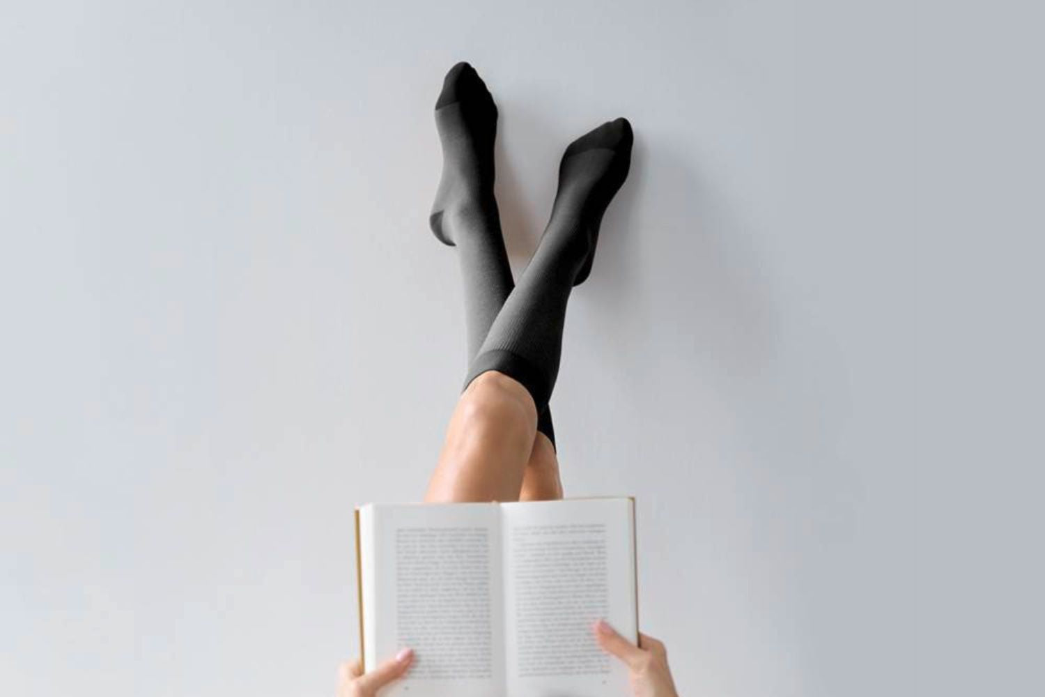 woman wearing Bauerfeind VenoTrain Cocoon Compression Socks while laying down reading with her legs in the air.