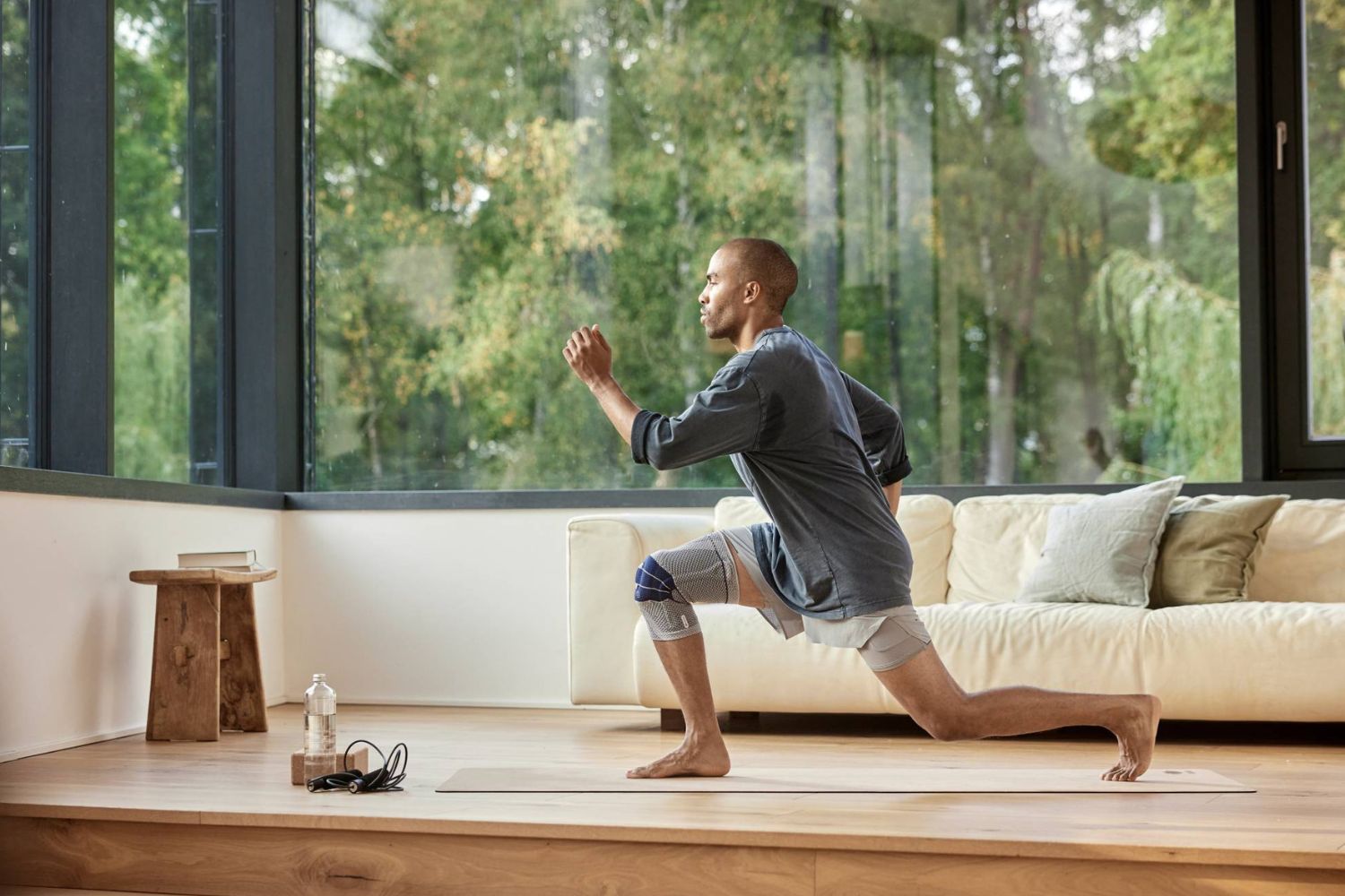 man doing lunges for knee pain in his living room. He is wearing Bauerfeind's GenuTrain Knee Support