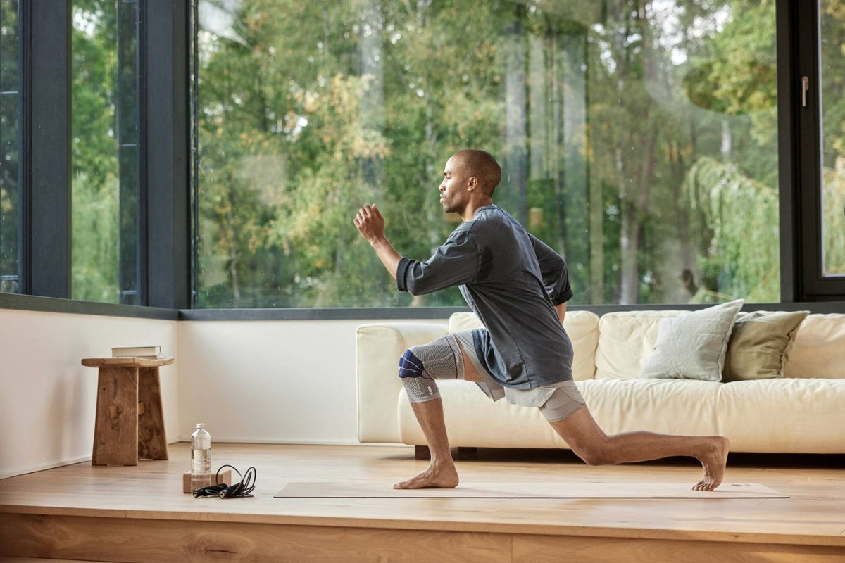 man doing lunges for knee pain in his living room. He is wearing Bauerfeind's GenuTrain Knee Support