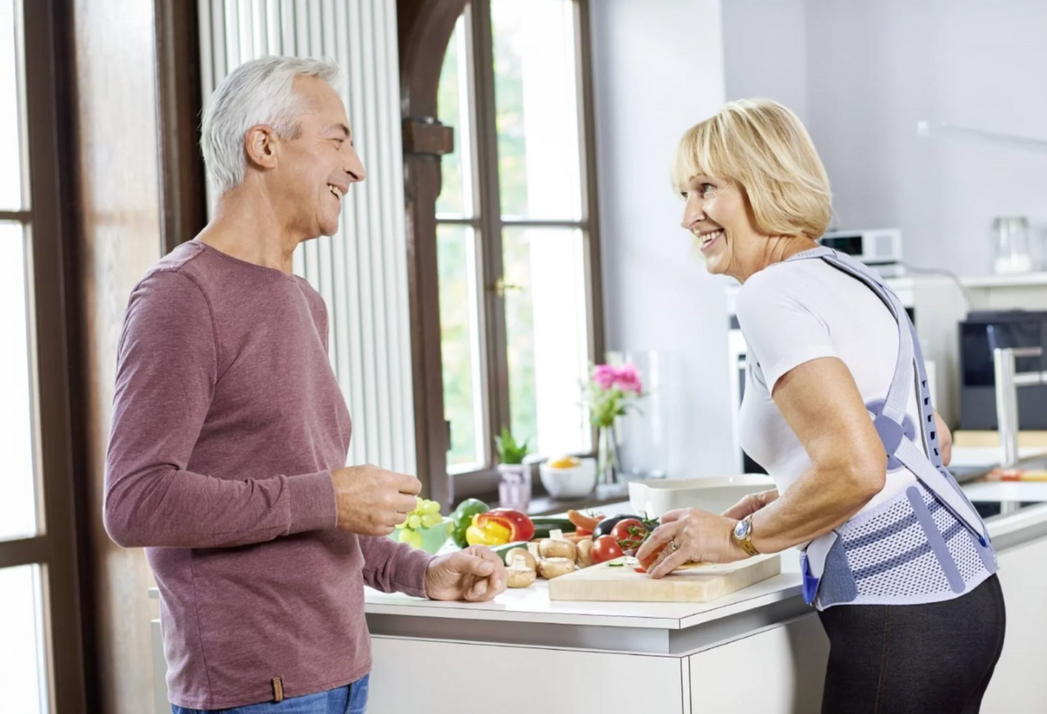 Older man and woman preparing food in the kitchen. The woman is wearing Bauerfeind Spinova to relieve back arthritis symptoms