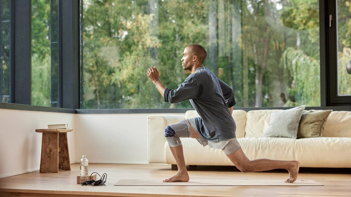 man doing lunges in his living room He is wearing Bauerfeind's GenuTrain Knee Brace