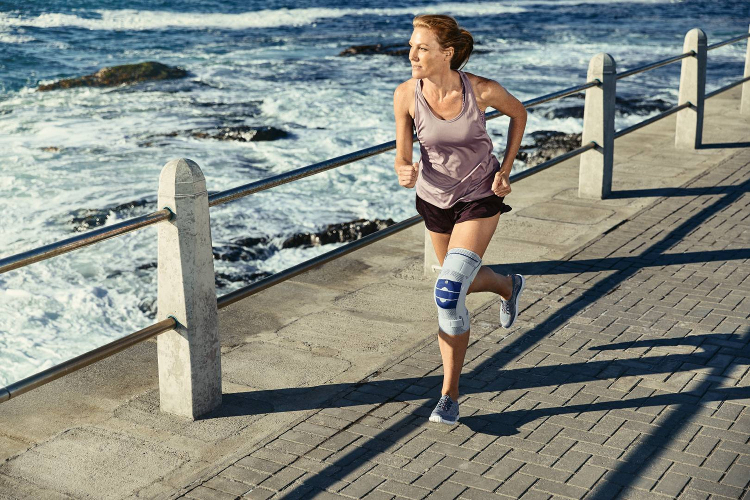 Woman with knee brace/support is running along on side-walk near the ocean