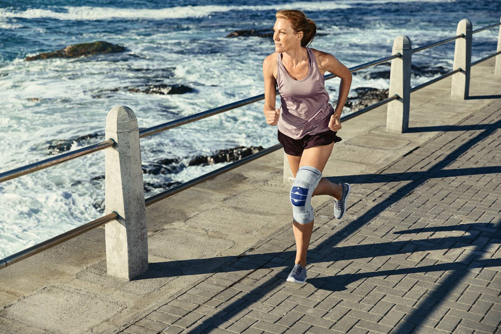 Woman with knee brace/support is running along on side-walk near the ocean