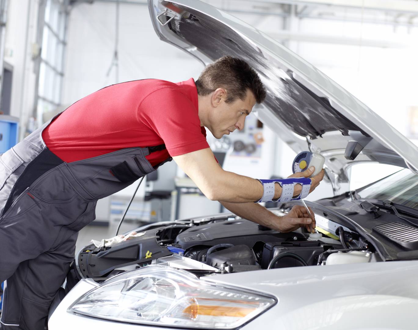 Mechanic repairing something under the hood of a grey car. He's wearing Bauerfeind's ManuLoc wrist brace for carpal tunnel