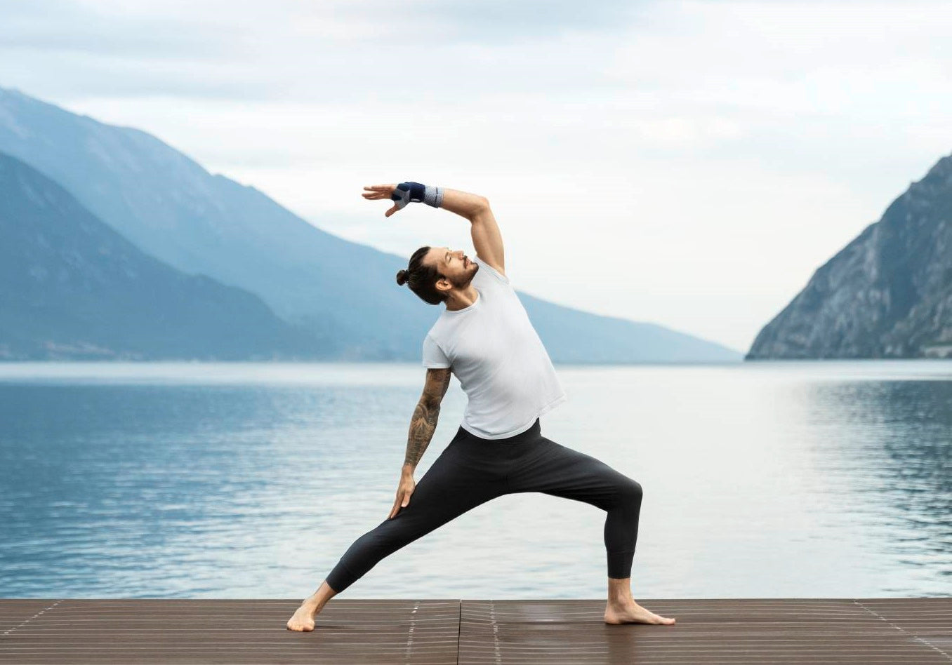 Man doing yoga on a deck by a lake. He's wearing a Bauerfeind ManuTrain wrist brace to support his sprained wrist as he exercises