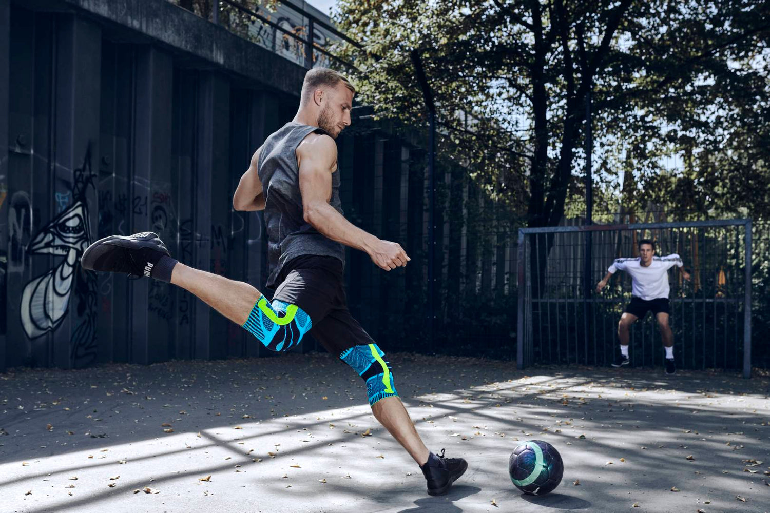 Man playing soccer with his freind. He's wearing Bauerfeind's Sports Knee Supports and about to kick the ball into the goal