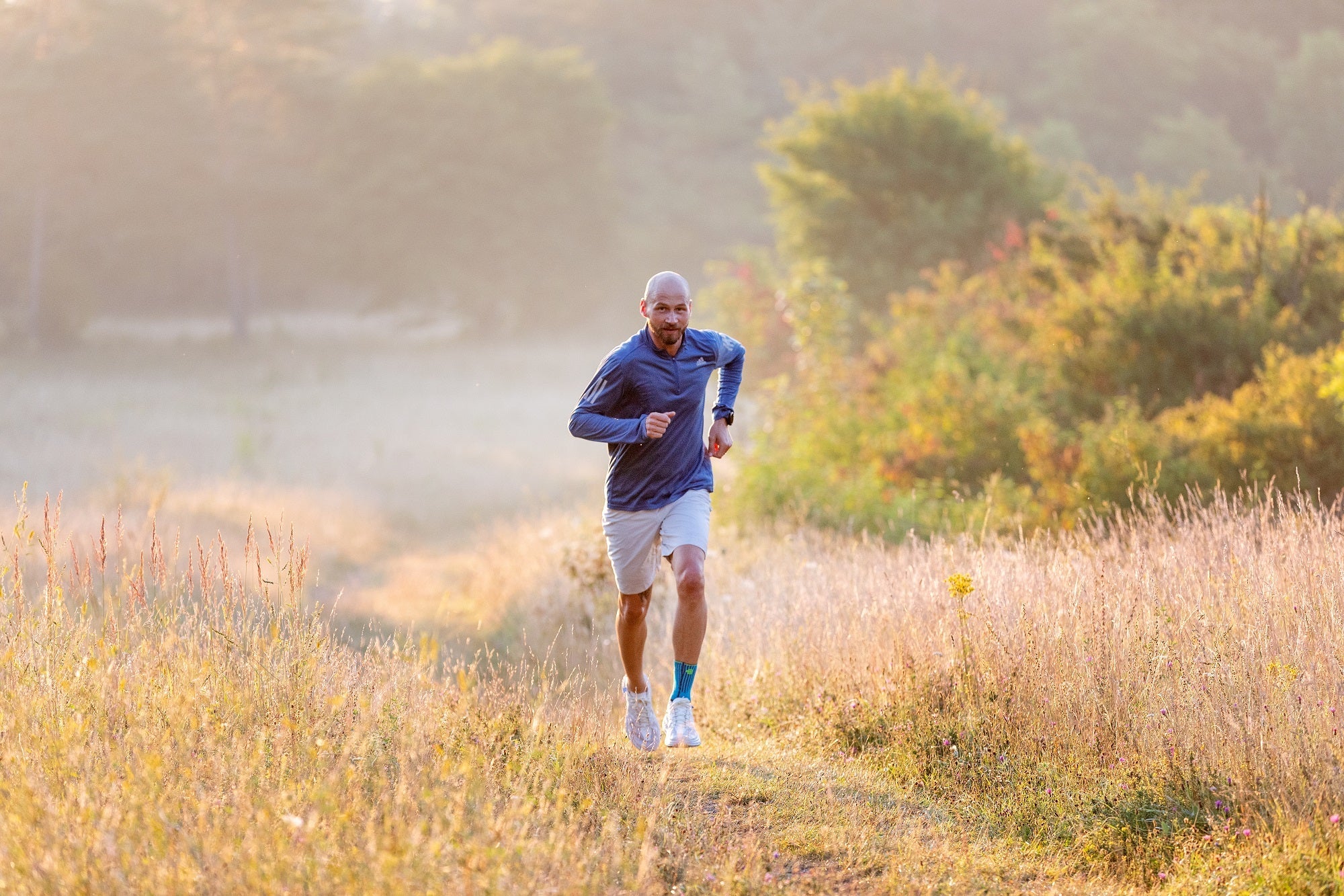 Man running across a yellow field. He's wearing a Bauerfeind sports ankle brace to help manage his ankle pain while running