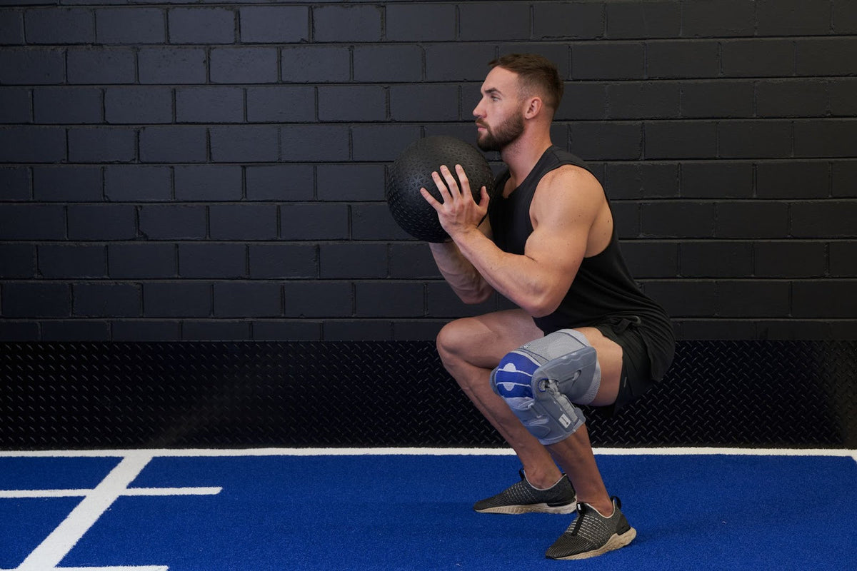 Man doing kettlebell squats at the gym. He's wearing Bauerfeind's SofTec Genu Knee Brace to relieve knee pain