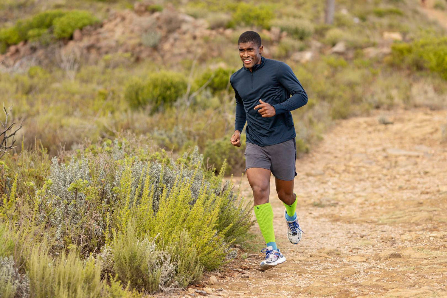 man running on a trail in performance socks. He seems to be experiencing discomfort, common to itb syndrome