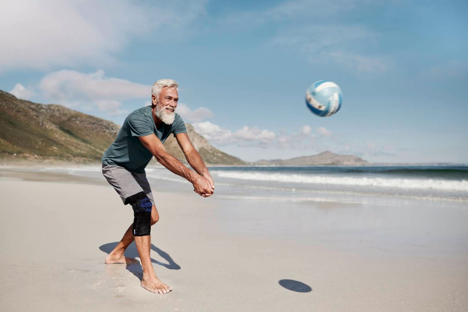 Older man playing volleyball at the beach. He is wearing Bauerfeind GenuTrain OA Knee Brace for osteoarthritis