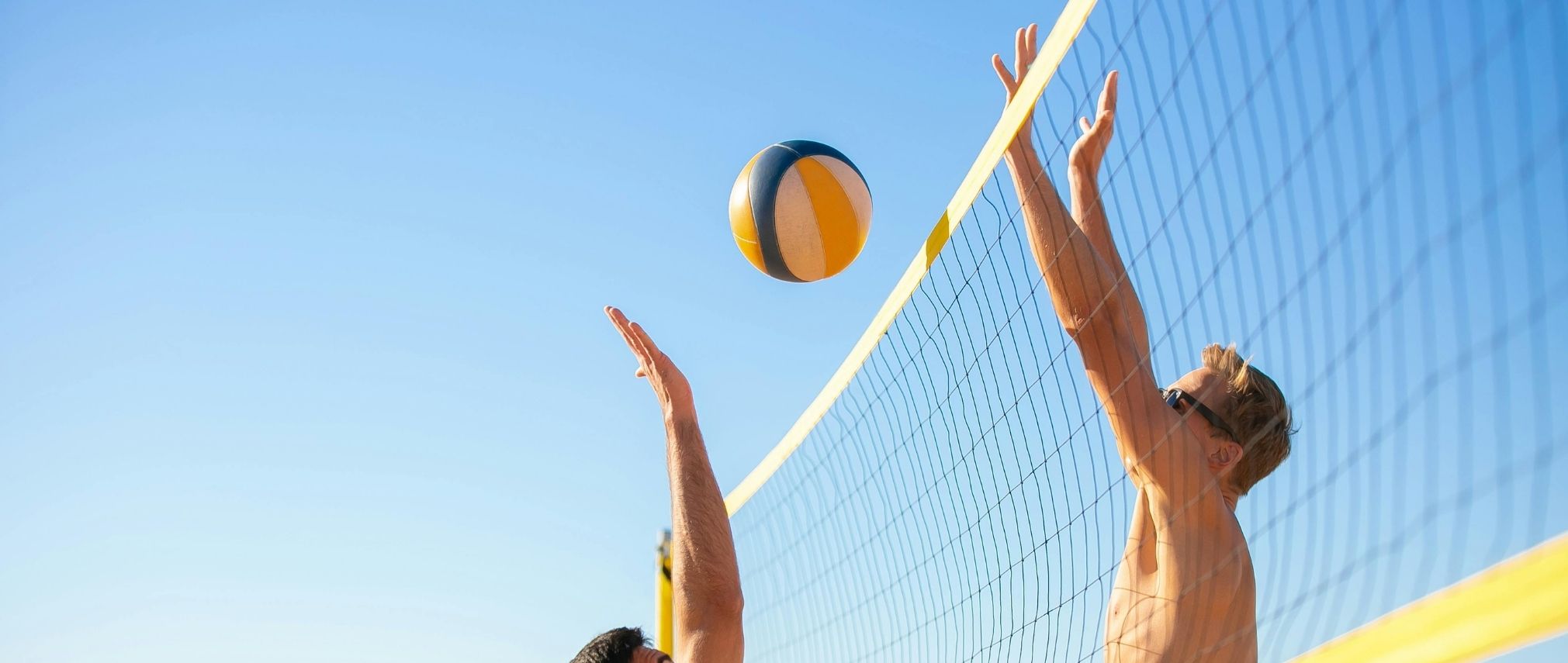 people playing volleyball. They are both trying to hit the ball over the net with their arms up and fingers splayed