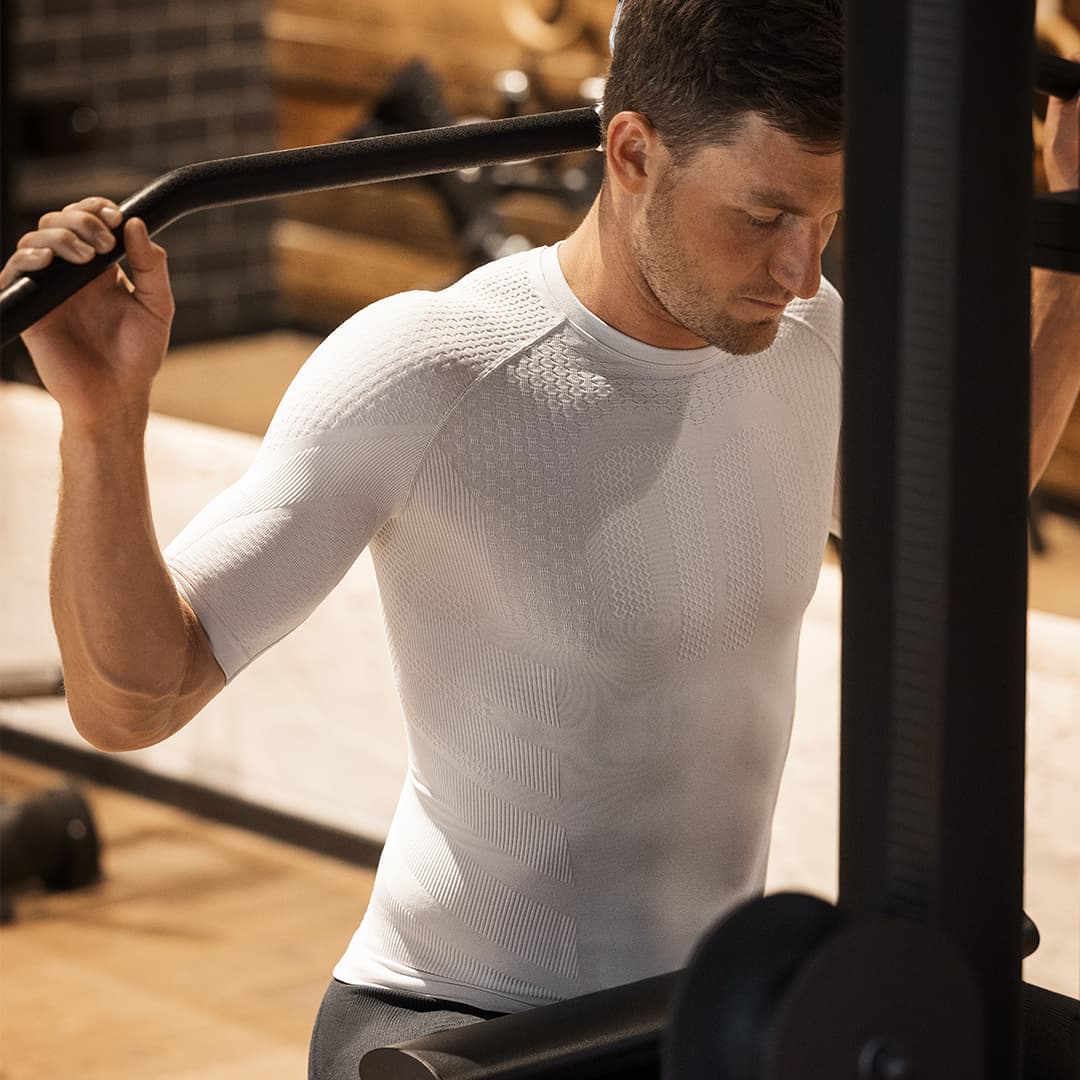 Man exercising on a cable machine in a gym setting wearing a silver-grey Bauerfeind compression shirt
