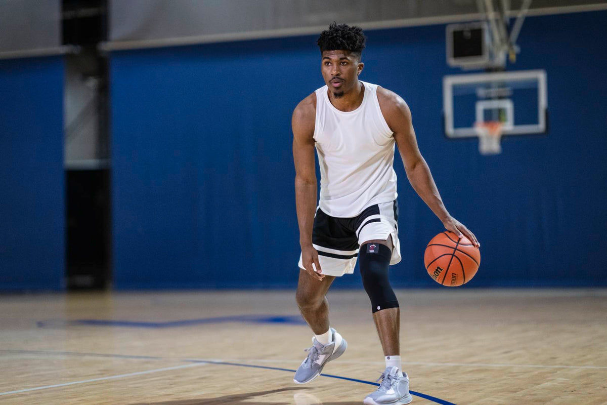 Man playing basketball in an indoor court. He is wearing Bauerfeind's NBA knee support to protect against common knee injuries in basketball