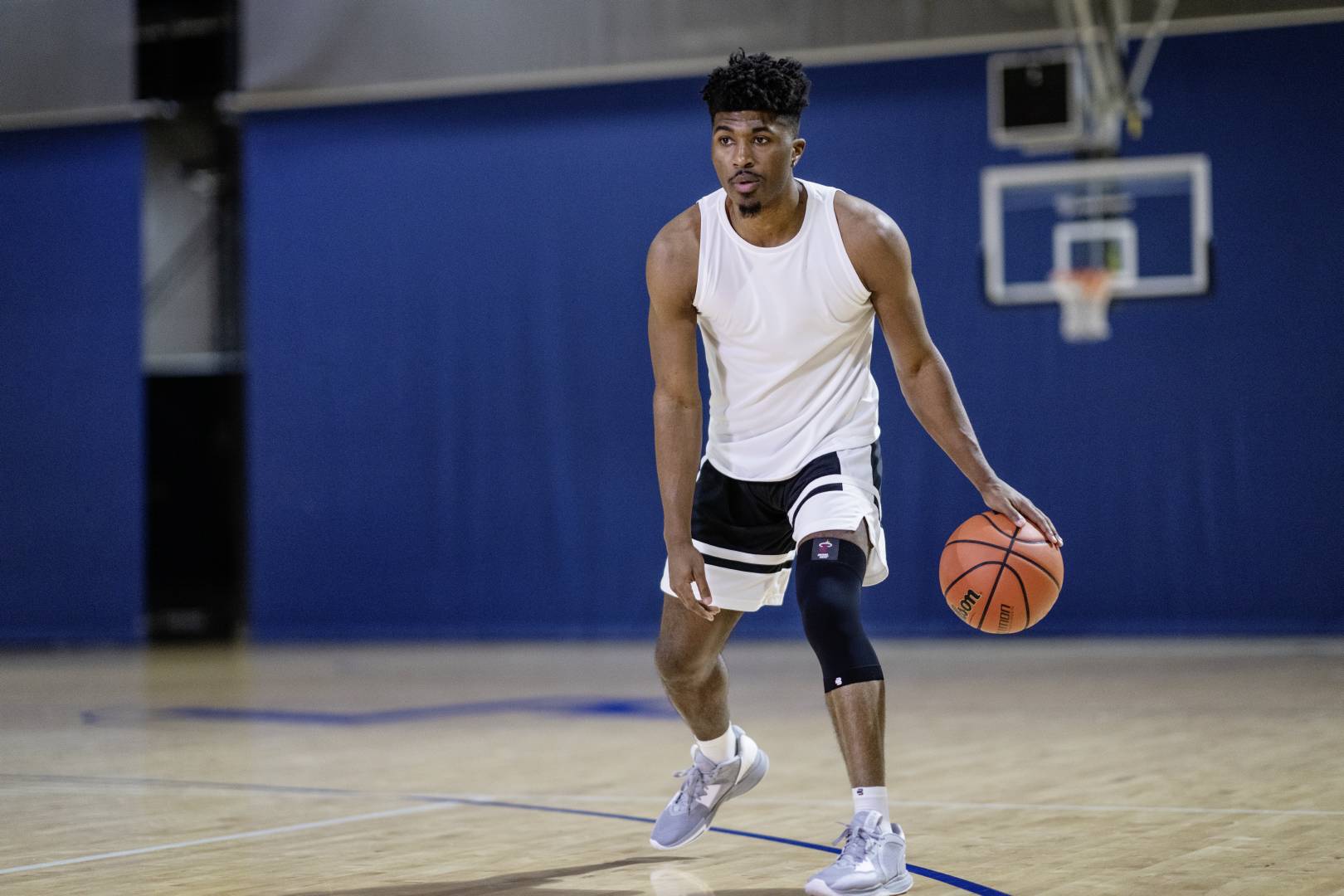 Man playing basketball in an indoor court. He is wearing Bauerfeind's NBA knee support to protect against common knee injuries in basketball