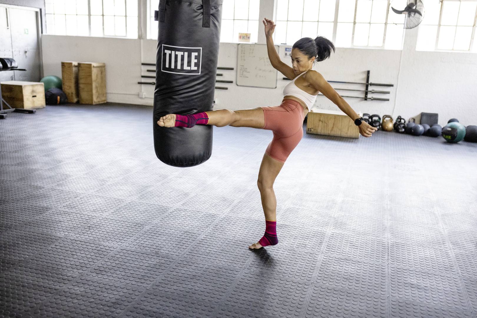 woman doing martial arts training. She is kicking a punching bag while wearing a sports compression ankle support