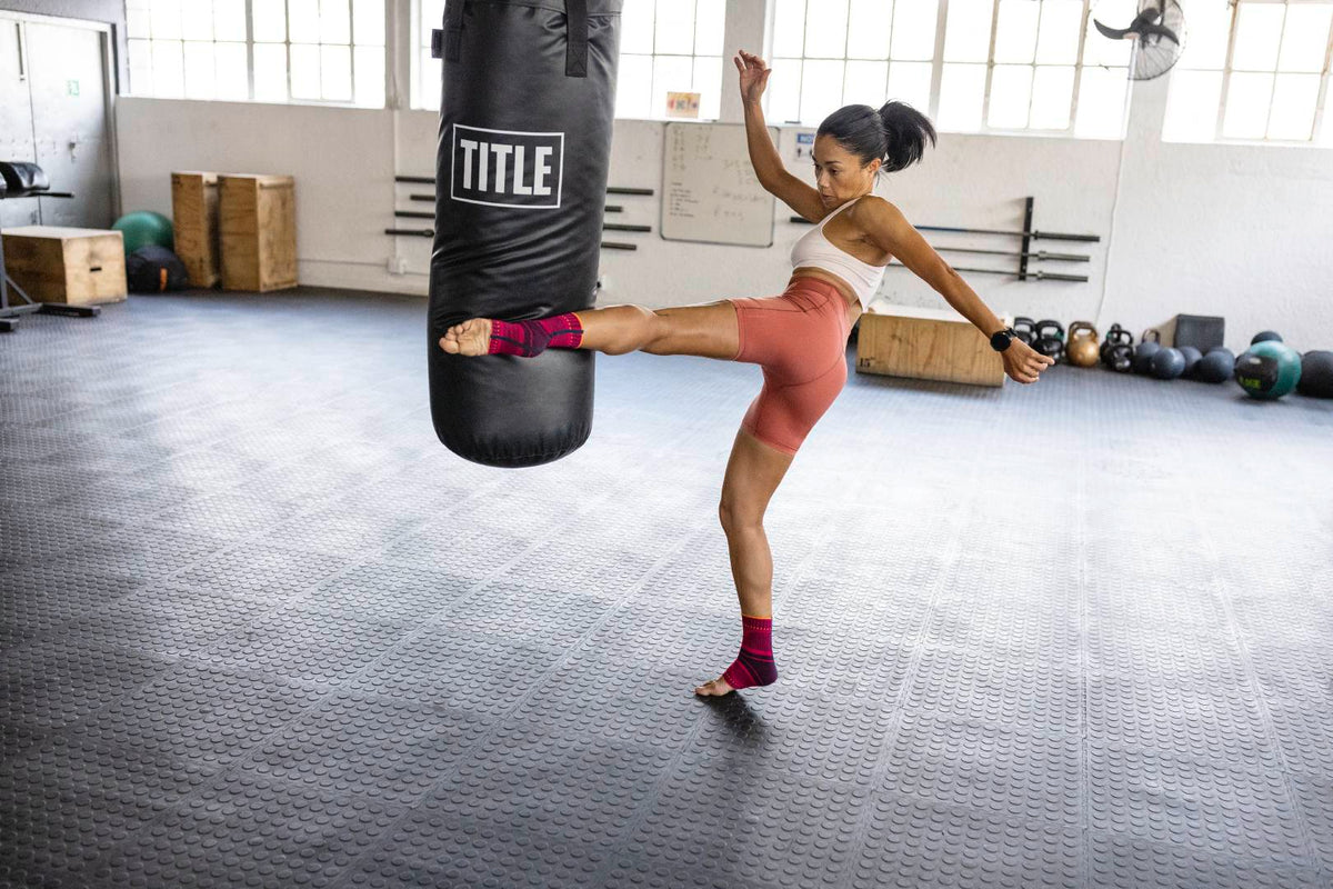 woman doing martial arts training. She is kicking a punching bag while wearing a sports compression ankle support