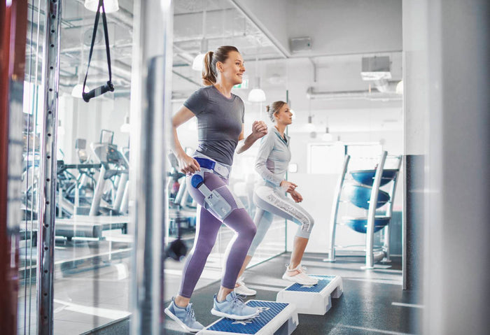 Two women at the gym doing the step ups exercise. One is wearing the CoxaTrain Hip Support for hip pain