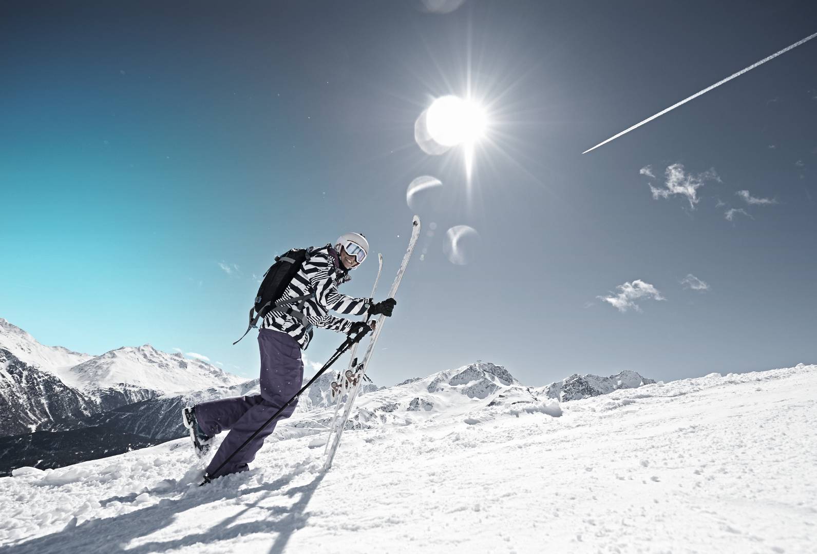 Ski beginner heading up a slope with her skis and ski poles in hand