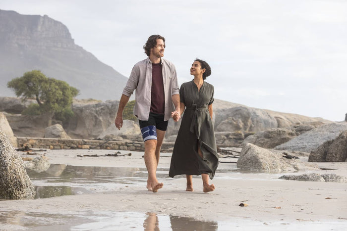 Man walking with his partner on the beach. He is wearing Bauerfeind's MyoTrain Thigh Brace to relieve thigh pain