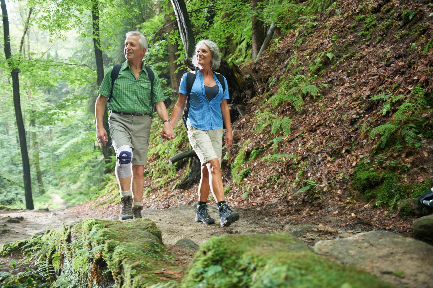 Couple walking through the woods on a hiking trail. One of them is wearing Bauerfeind's GenuTrain P3 Knee Support to relieve runner's knee pain