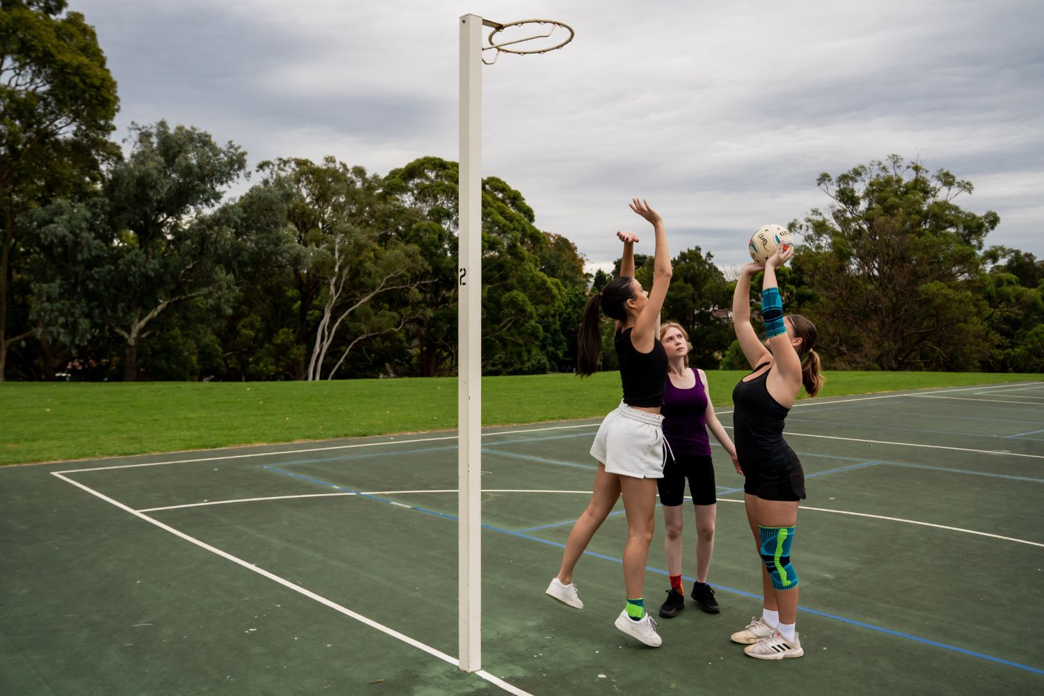 women playing netball on a court at the park. One of them is wearing Bauerfeind's Sports Knee Support