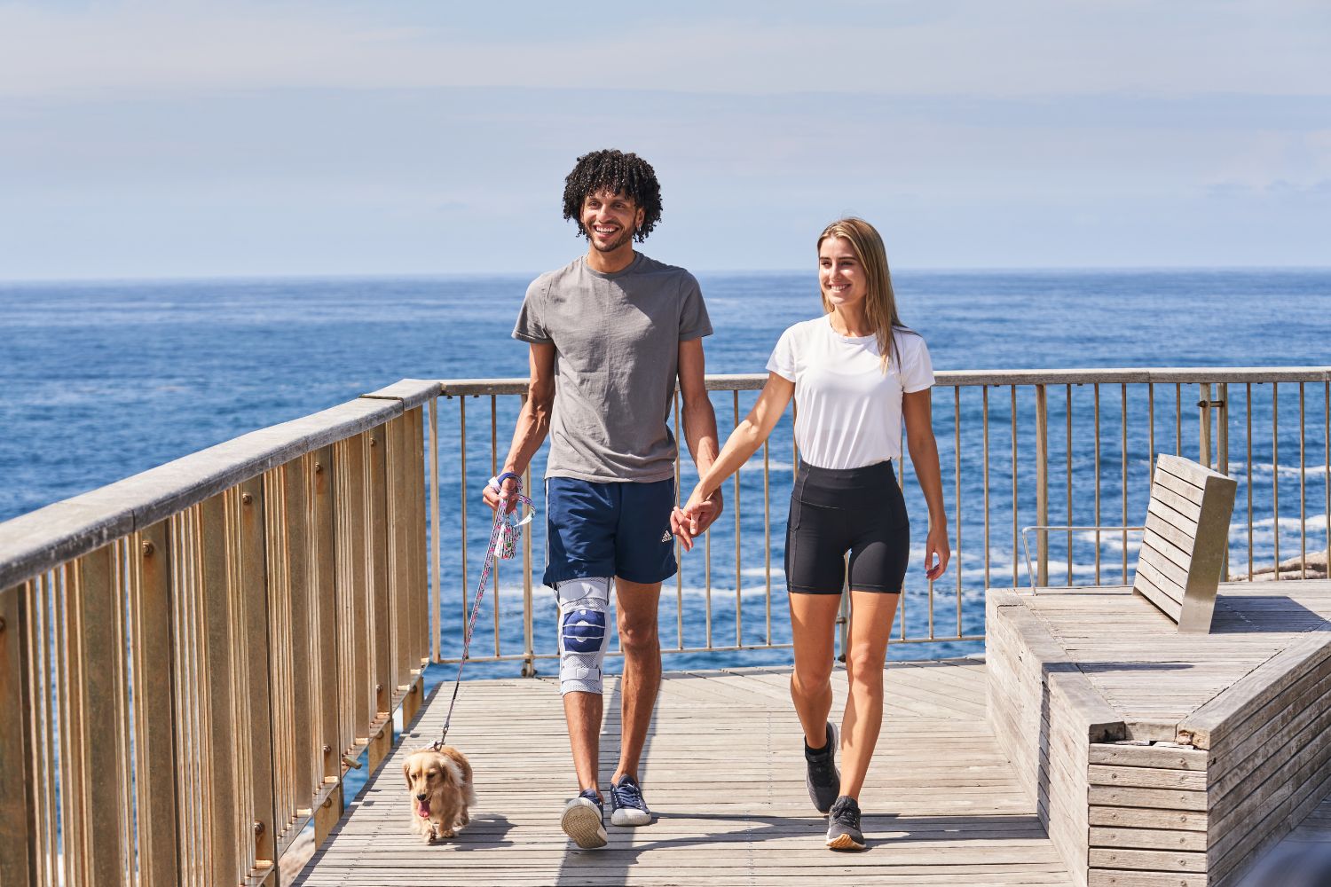 man and woman walking their dog on a cliff walk. The man is wearing Bauerfeind's GenuTrain S Knee Brace for ligament injury