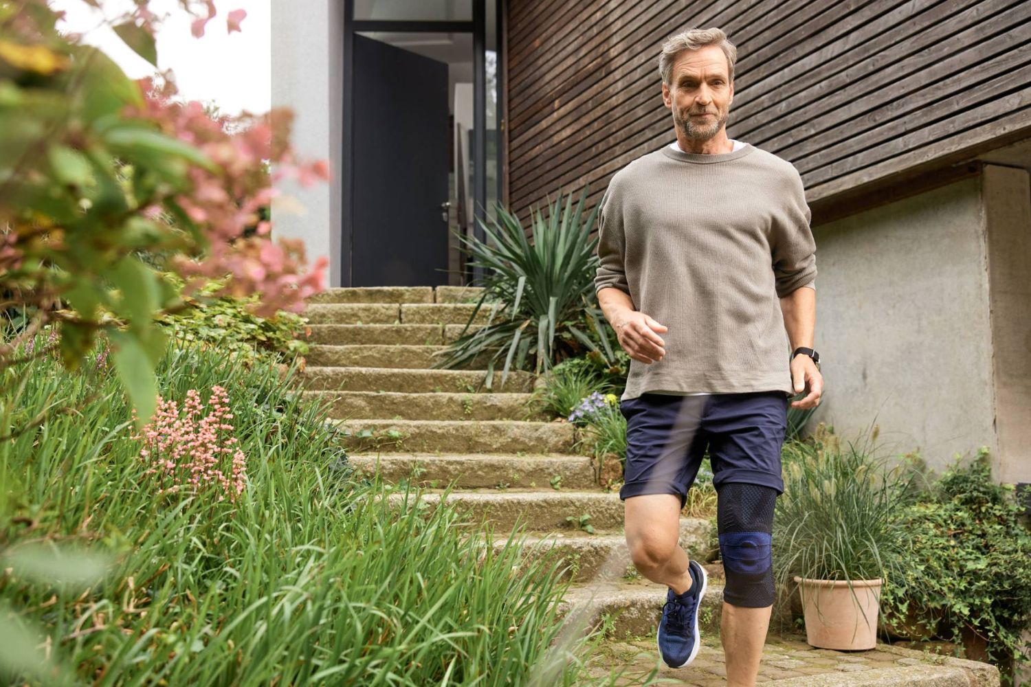 man walking down the stairs to his house in Bauerfeind's GenuTrain Knee Brace, which he is not wearing with pants but with shorts
