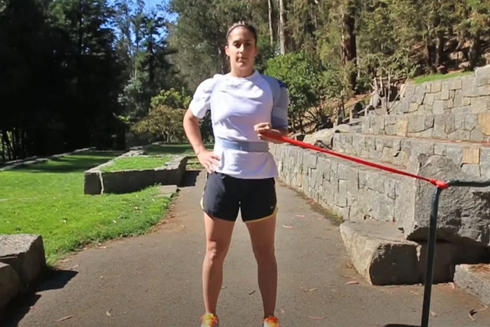 Woman doing internal shoulder rotations at the park. She is wearing the OmoTrain Shoulder Support