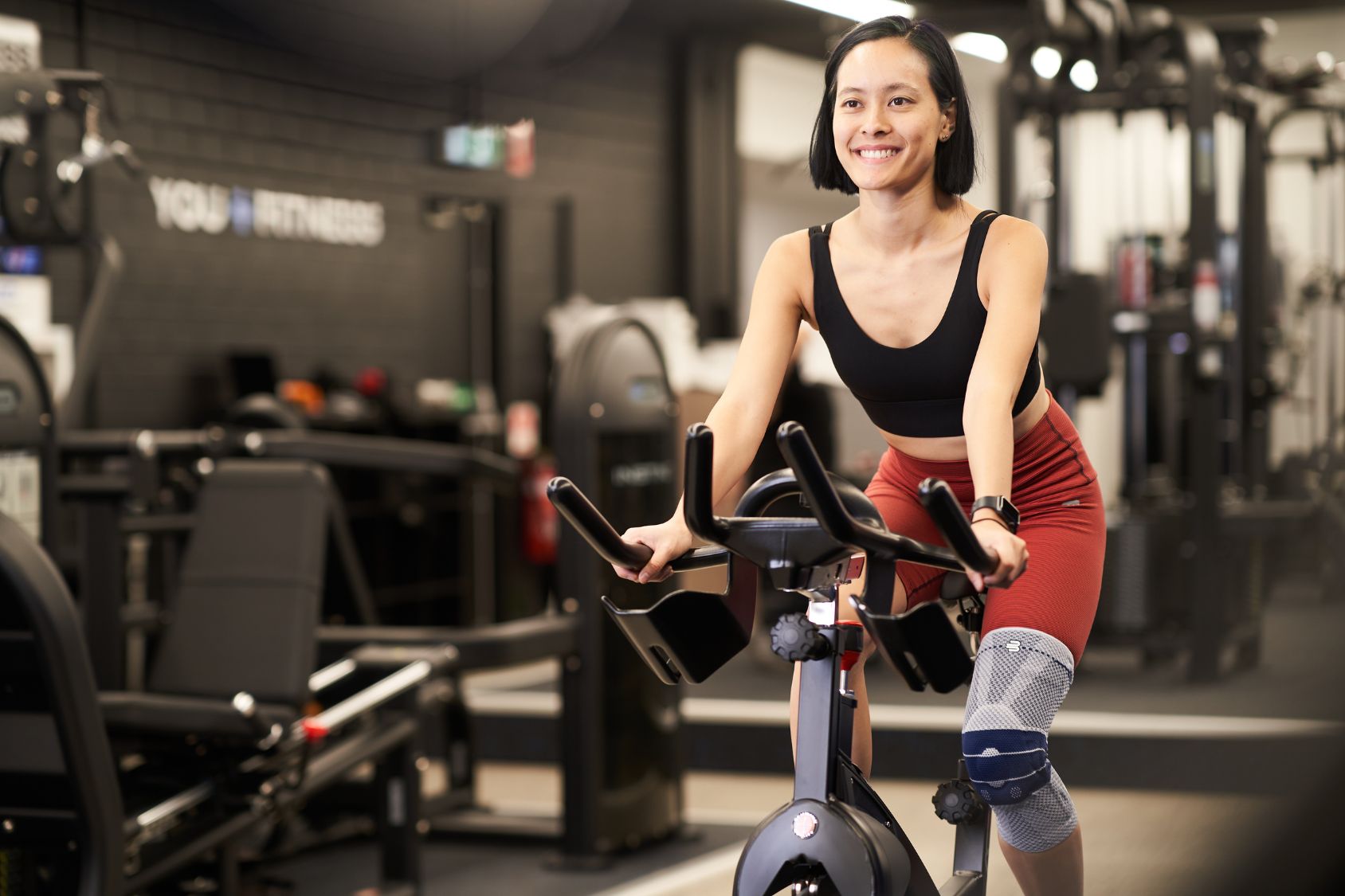 woman on an exercise bike. She is wearing Bauerfeind's GenuTrain Knee Support