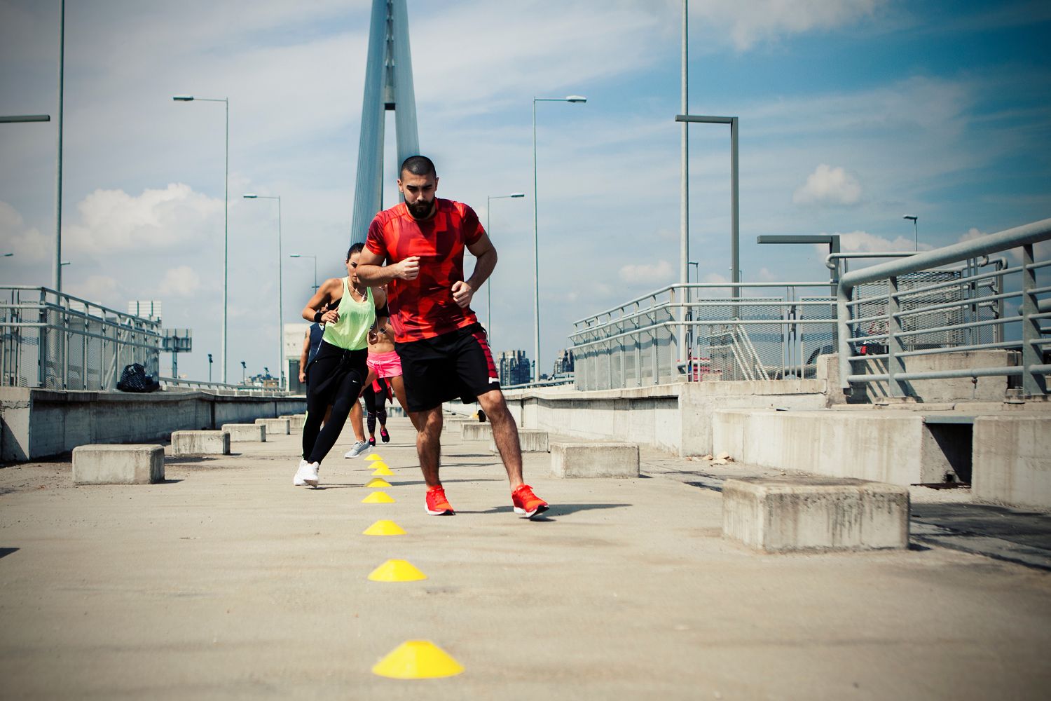 people doing agility training at a concrete park. They are running side to side between some cones