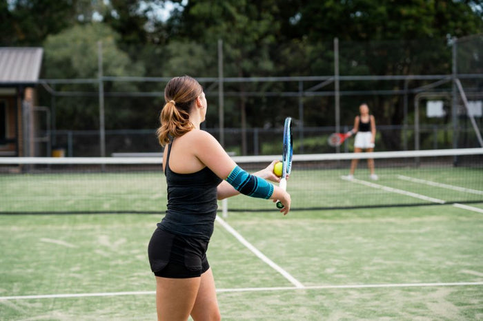 woman playing tennis. She is wearing Bauerfeind's Sports Elbow Support. It has moisture wicking knit for comfort