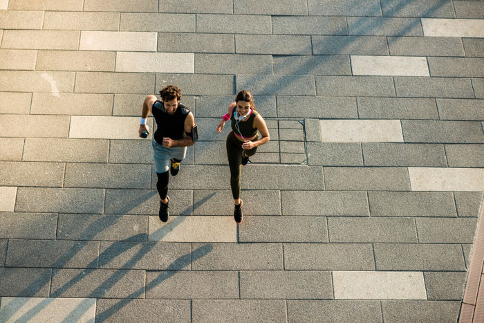 Aerial image of a man and woman running on the street. The ground under them is stone tile