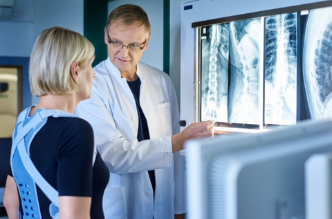 Doctor showing patient, who is wearing a Bauerfeind back brace, her spinal x-ray.