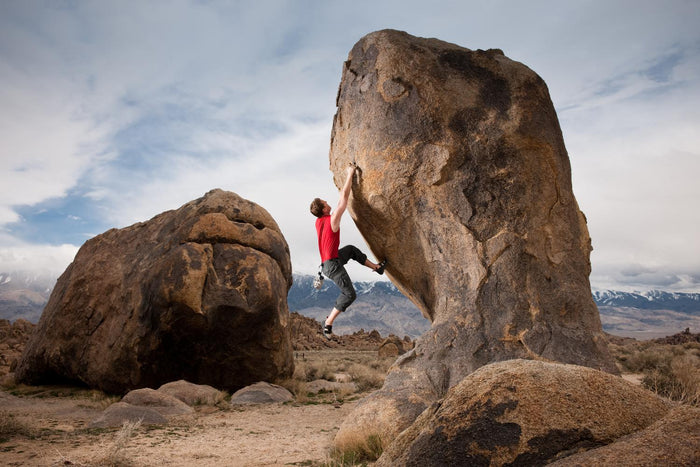 Man Bouldering. He is about halfway up a tall boulder