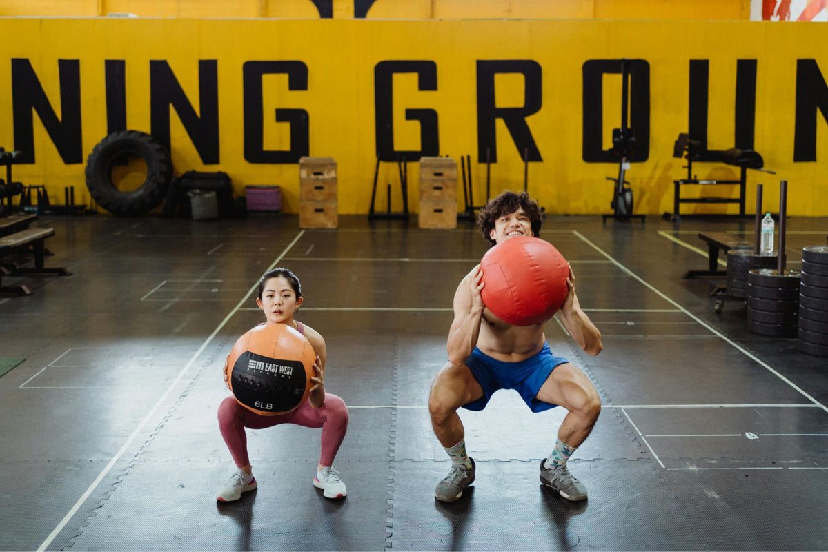 man and woman doing sumo squats at the gym. They are holding weighted gym balls for more resistance