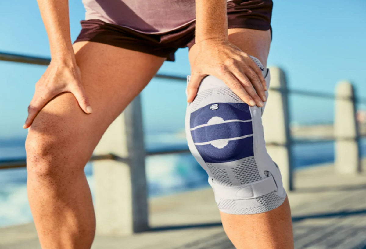 Person at the beach resting their hands on their knees to rest after a walk or run. They're wearing a Bauerfeind knee brace to relieve knee arthritis symptoms