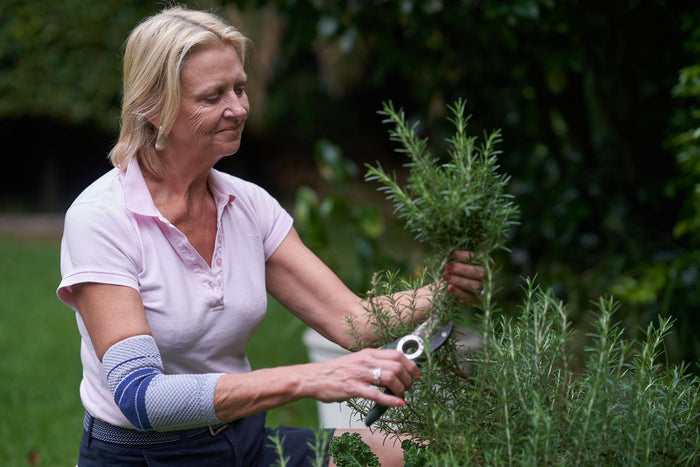 Woman pruning a shrub with garden shears. She's wearing the EpiTrain Elbow Brace to avoid gardening pain