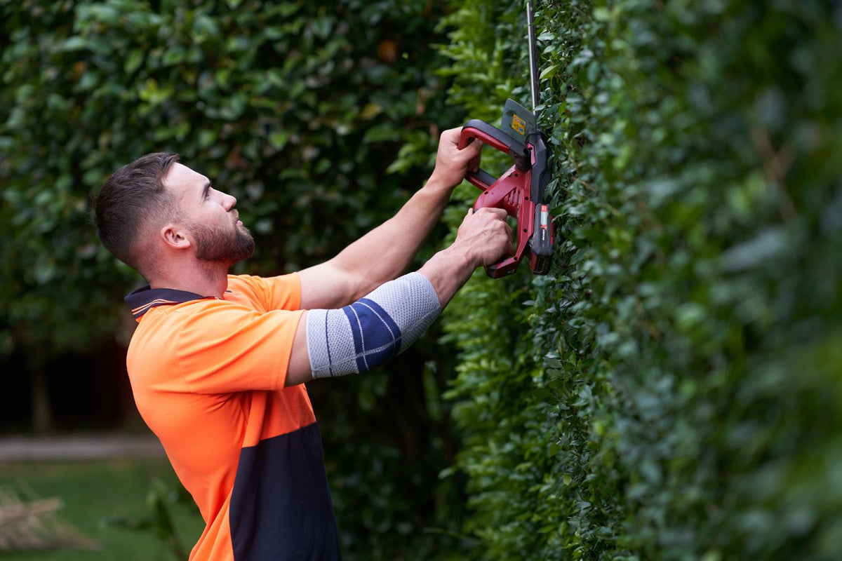Man trimming a hedge in EpiTrain Elbow Brace to avoid Garderner's Elbow pain