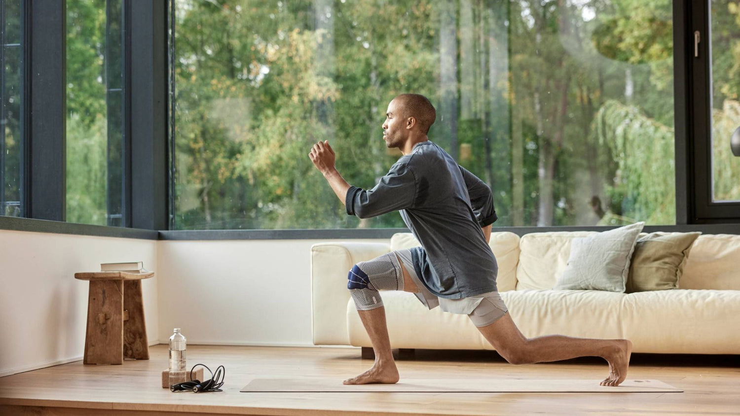 man doing lunges in his living room He is wearing Bauerfeind's GenuTrain Knee Brace