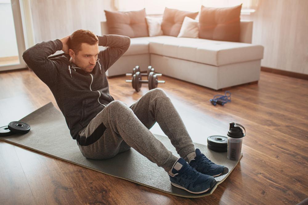 The at-home Workout Guide. Man is sitting on the floor of his living room, doing sit ups