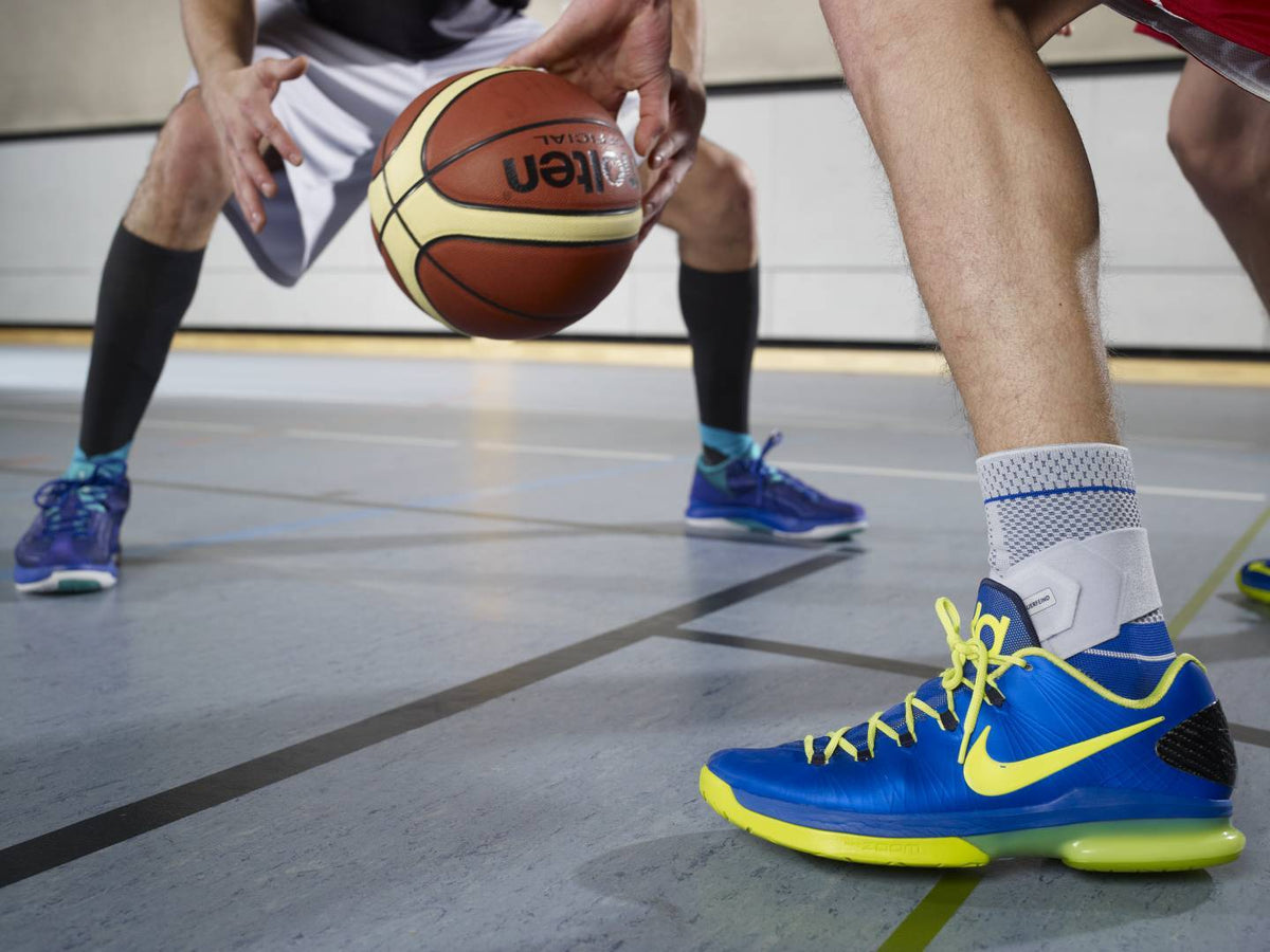 Image of two men playing basketball, one man is wearing a Bauerfeind ankle brace. Image relates to blog post with tips for selecting the right ankle brace for your injury