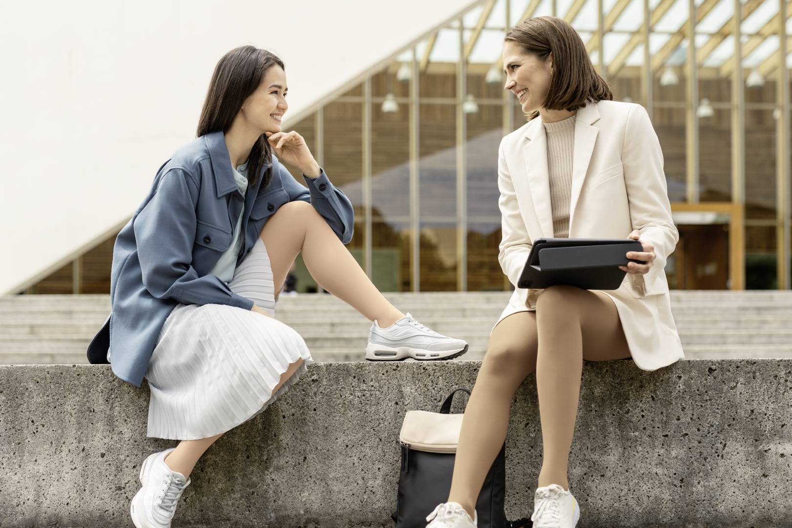 two women sitting on a stone bench in work attire/ One is wearing compression socks