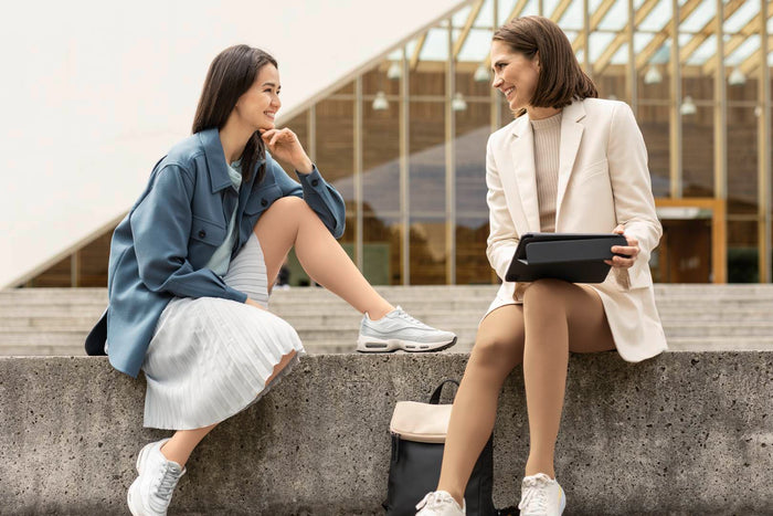 two women sitting on a stone bench in work attire/ One is wearing compression socks