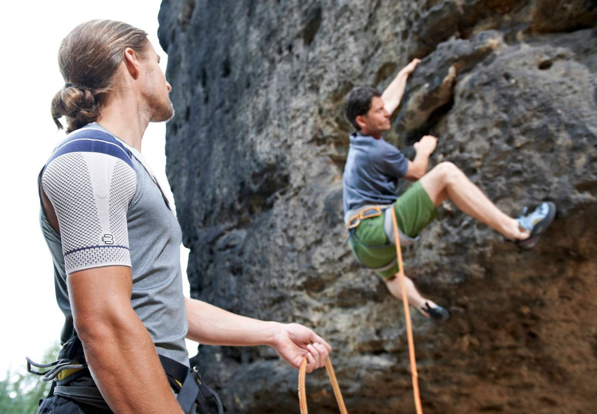Man holding the rope for his friend while he mountain climbs. The man is wearing an OmoTrain S Shoulder Brace to manage shoulder pain 