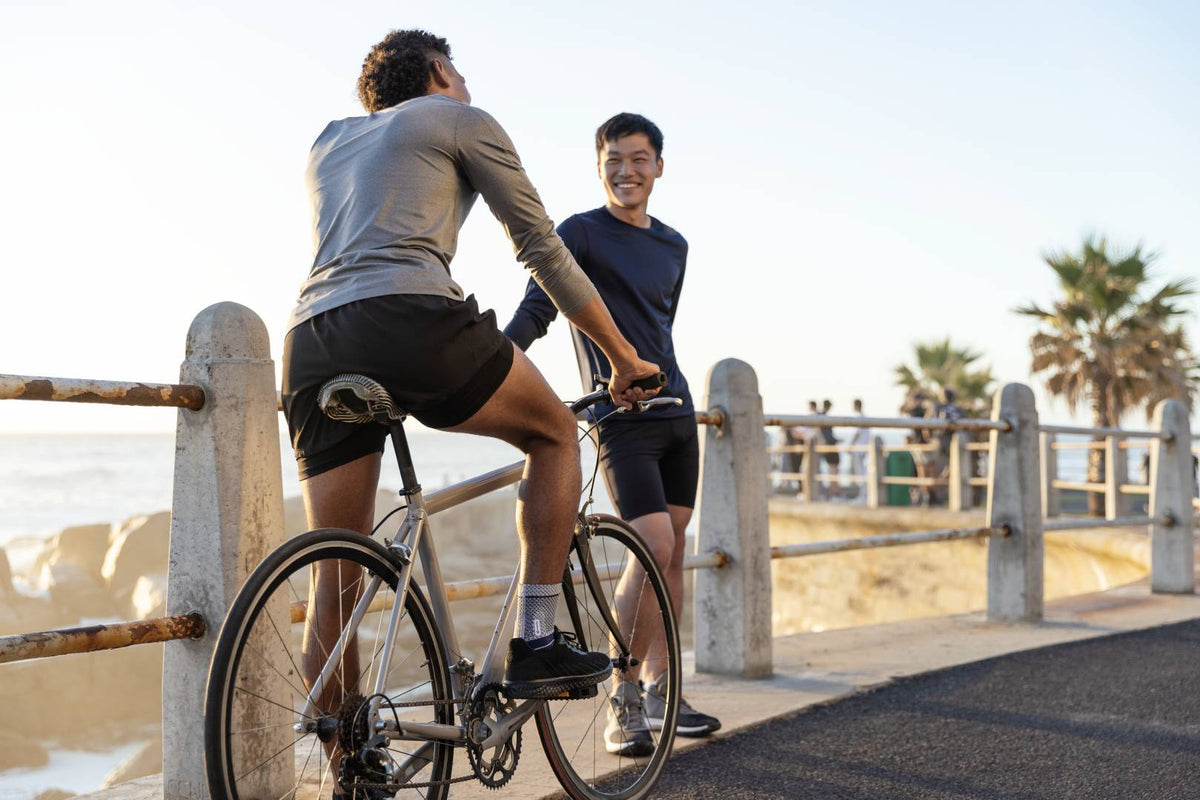 Man talking to his friend at the beach. The man is on a bicycle and is wearing a Bauerfeind MalleoTrain ankle brace, both good ways to manage ankle arthritis pain and other symptoms