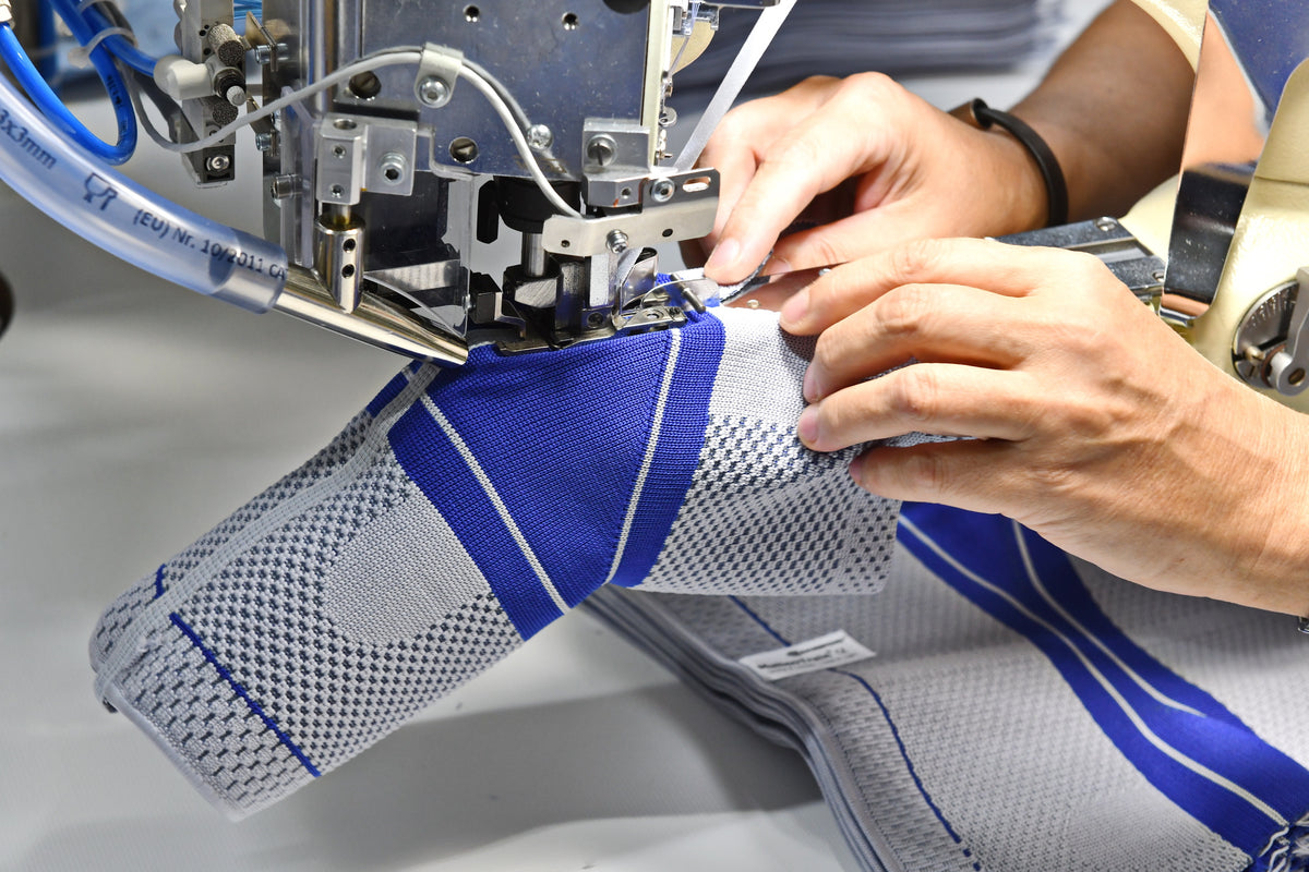 Bauerfeind Technician running a GenuTrain Knee Brace through a sewing machine to stitch on the knee brace's patella pad