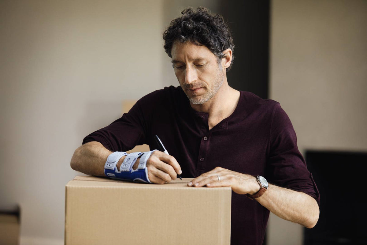 Man with writing something on a moving box. He is wearing Bauerfeind's ManuLoc wrist brace to help manage wrist pain