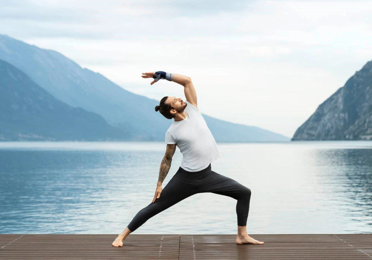 Man doing yoga on a deck by a lake. He's wearing a Bauerfeind ManuTrain wrist brace to support his sprained wrist as he exercises 