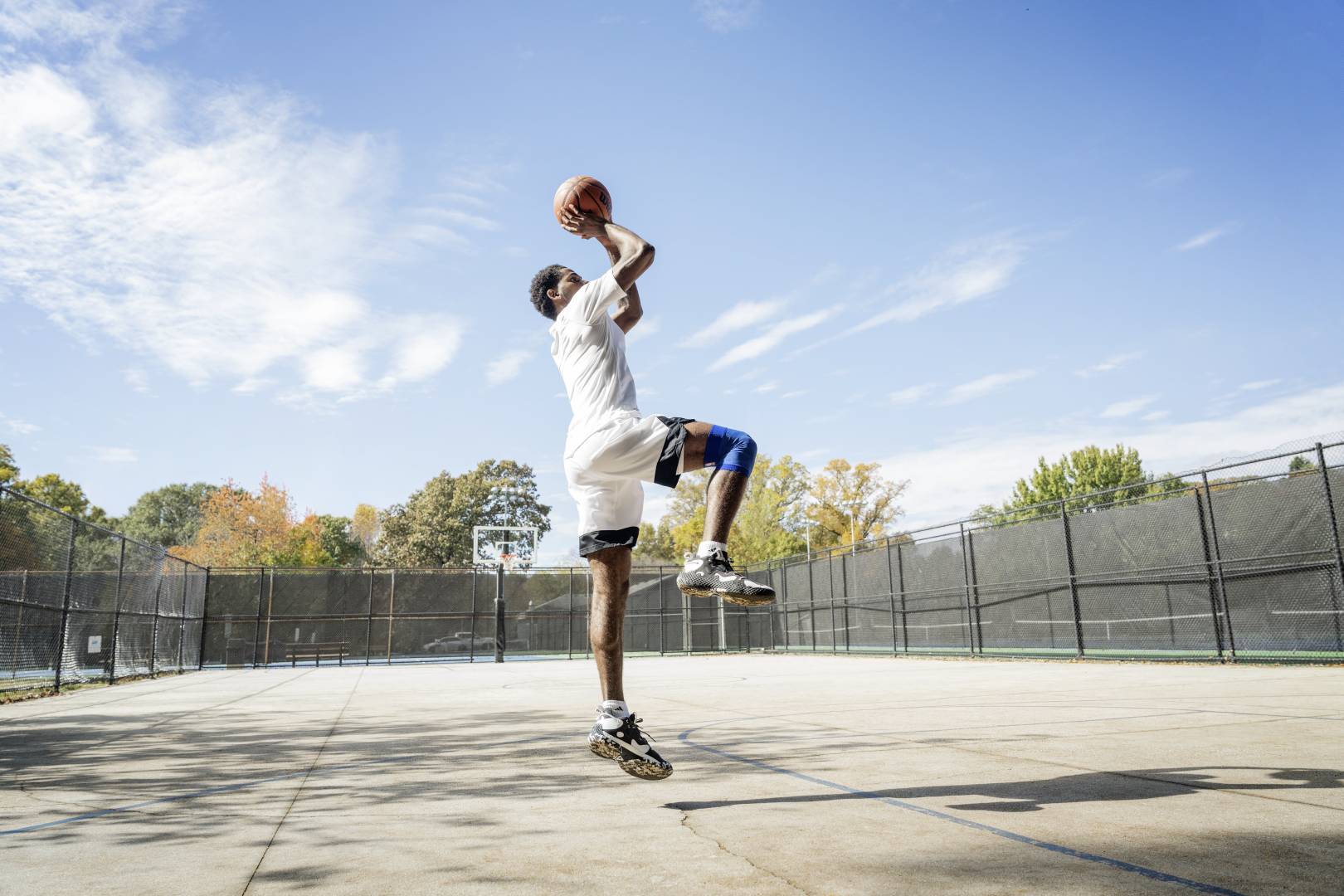 Basketball player jumping up and aiming to take a shot. He's wearing basketball shoes and Bauerfeind NBA Compression Knee Support, great basketball training gear 