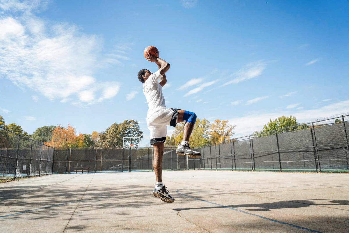 Basketball player jumping up and aiming to take a shot. He's wearing basketball shoes and Bauerfeind NBA Compression Knee Support, great basketball training gear 